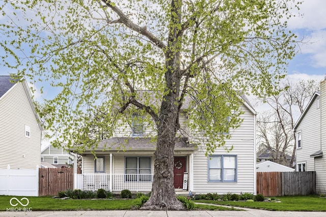 view of front of home with roof with shingles, a front yard, covered porch, and fence