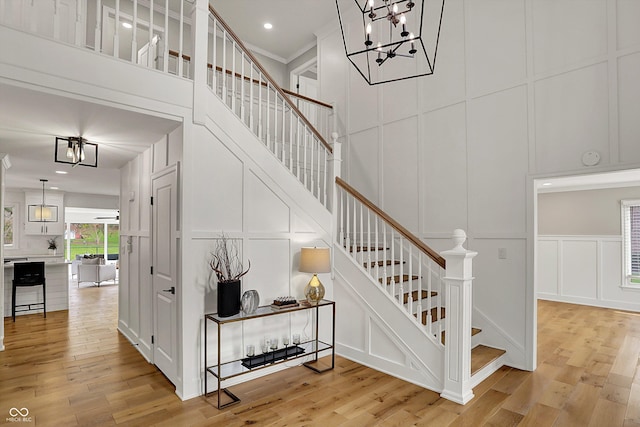 stairs featuring a towering ceiling, recessed lighting, a notable chandelier, wood finished floors, and a decorative wall