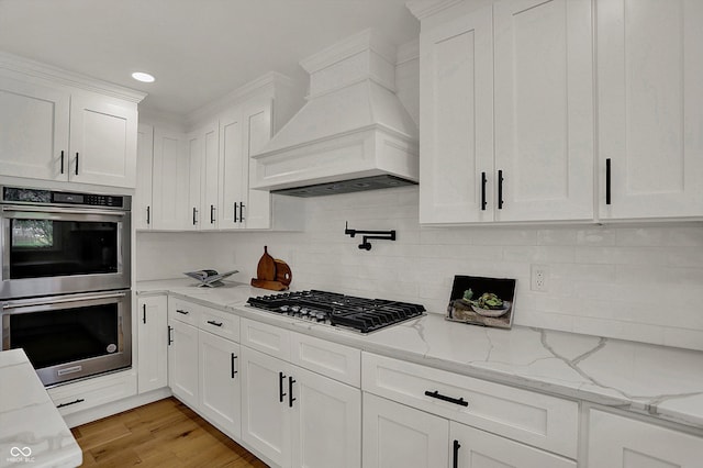 kitchen with premium range hood, backsplash, white cabinets, and stainless steel appliances