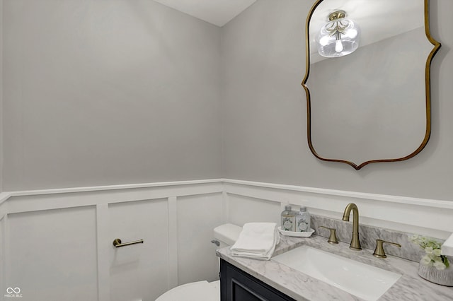 bathroom with wainscoting, toilet, vanity, and a decorative wall