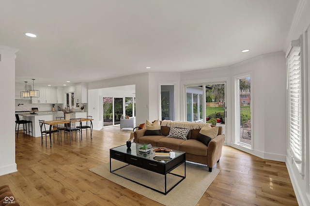 living room with light wood finished floors, baseboards, recessed lighting, and ornamental molding