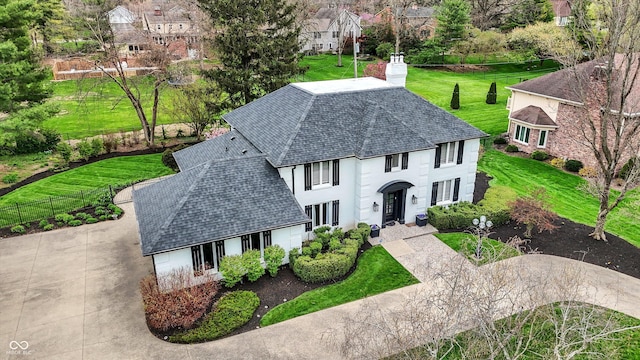 view of front facade with a chimney, a front lawn, fence, roof with shingles, and a residential view