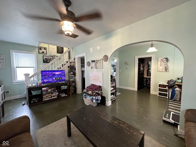 living room with arched walkways, baseboards, a ceiling fan, and stairs