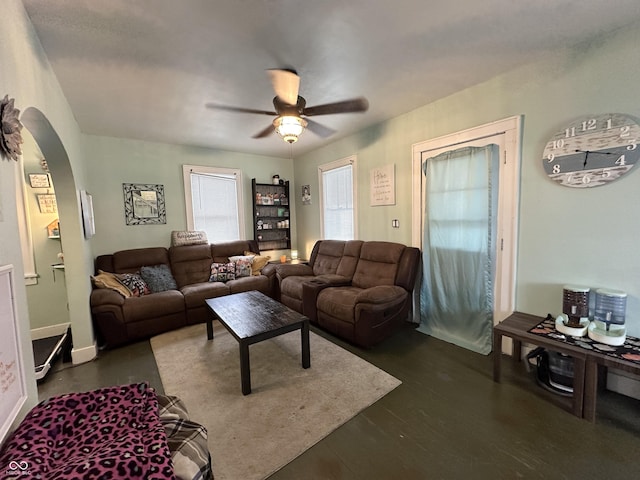 living area with arched walkways, ceiling fan, and dark wood-style floors