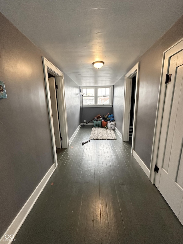 corridor featuring dark wood-type flooring and baseboards