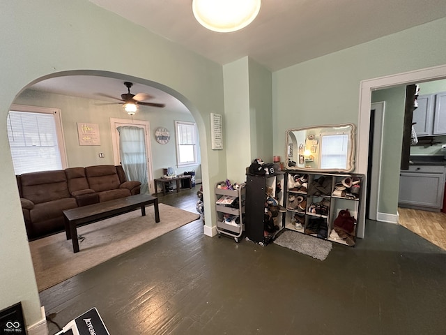 living area with arched walkways, baseboards, wood finished floors, and ceiling fan