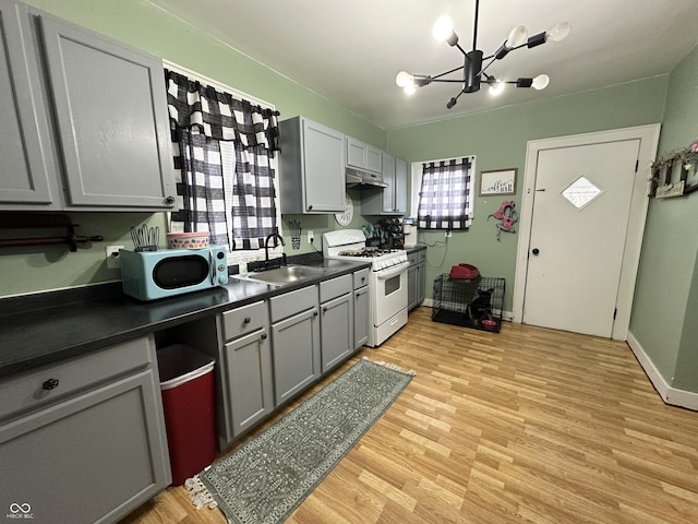 kitchen featuring a notable chandelier, dark countertops, white range with gas stovetop, light wood finished floors, and a sink