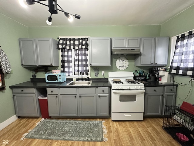 kitchen featuring gray cabinets, dark countertops, gas range gas stove, under cabinet range hood, and a sink