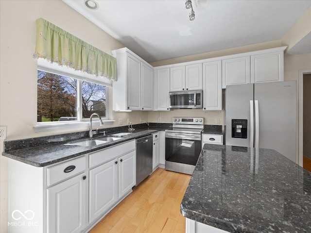 kitchen with white cabinets, light wood-style floors, stainless steel appliances, and a sink