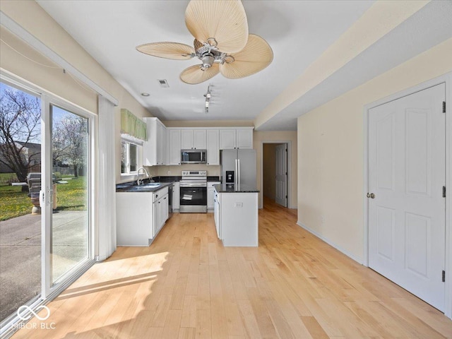 kitchen featuring a sink, dark countertops, white cabinets, light wood-type flooring, and appliances with stainless steel finishes