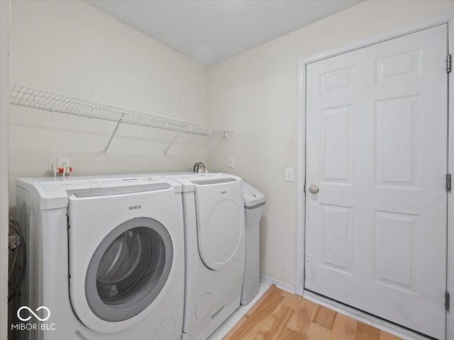 clothes washing area with washing machine and dryer, laundry area, baseboards, and light wood-style floors
