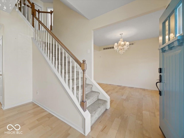 foyer with an inviting chandelier, wood finished floors, visible vents, baseboards, and stairs