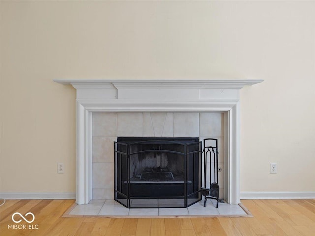 interior details with a tiled fireplace, wood finished floors, and baseboards