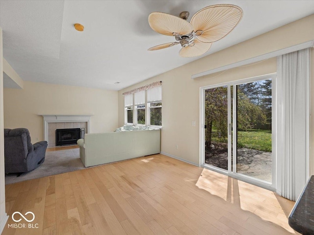 unfurnished living room with a ceiling fan, light wood finished floors, and a tiled fireplace