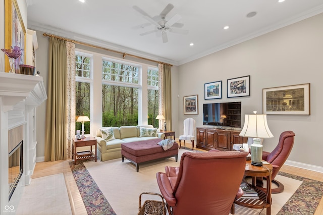 living area featuring crown molding, light wood-style floors, baseboards, ceiling fan, and a premium fireplace