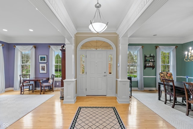 foyer featuring crown molding, decorative columns, an inviting chandelier, and light wood-type flooring