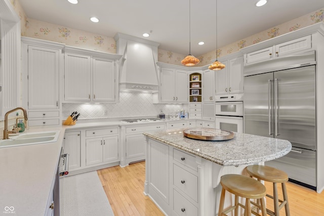 kitchen with white appliances, light wood finished floors, a sink, and custom range hood