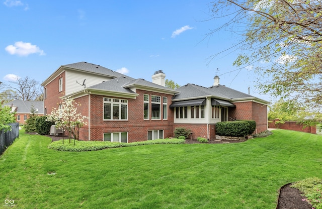 back of property featuring fence, a lawn, and brick siding