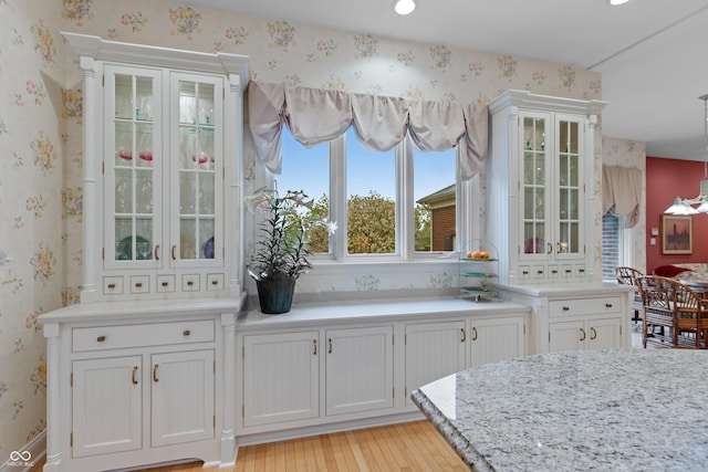 kitchen with light wood-style floors, glass insert cabinets, wallpapered walls, and white cabinetry