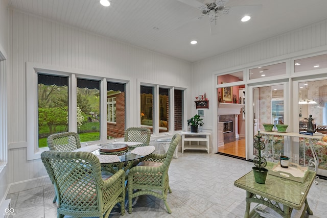 sunroom with outdoor dining area, ceiling fan, and a glass covered fireplace