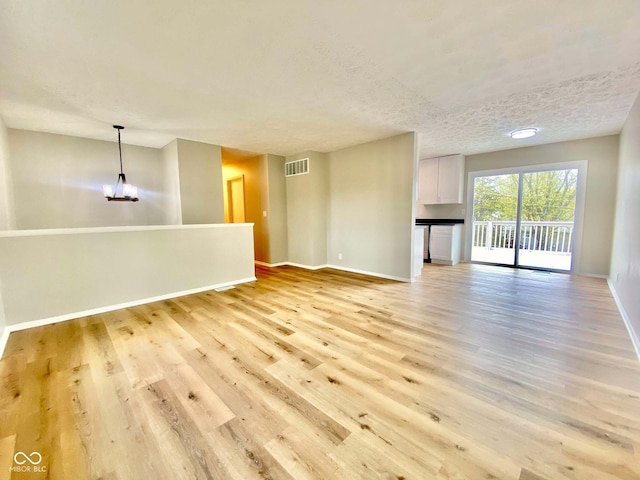110 Renee Dr, Ellettsville, IN 47429 - unfurnished living room with light wood-style floors, a textured ceiling, and a chandelier