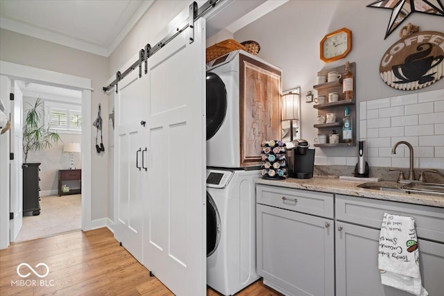 7638 Beekman Ter, Zionsville, IN 46077 - laundry room with a barn door, stacked washer / dryer, light wood-type flooring, and ornamental molding
