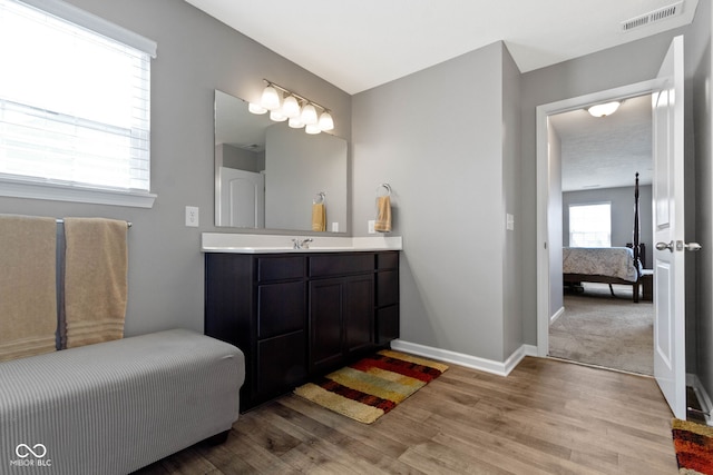 ensuite bathroom with vanity, baseboards, wood finished floors, ensuite bathroom, and visible vents