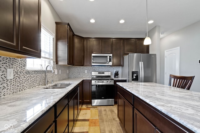 kitchen featuring dark brown cabinetry, light stone counters, a sink, light wood-style flooring, and stainless steel appliances
