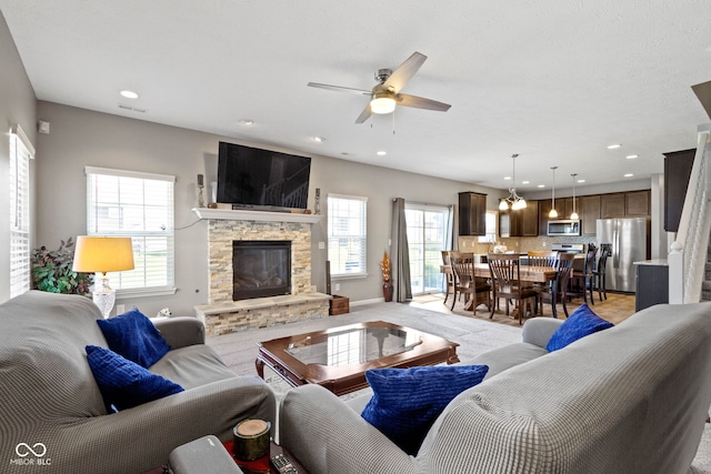 living area featuring a stone fireplace, recessed lighting, plenty of natural light, and ceiling fan
