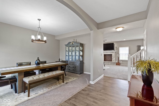 dining room featuring light carpet, baseboards, a stone fireplace, light wood-type flooring, and arched walkways