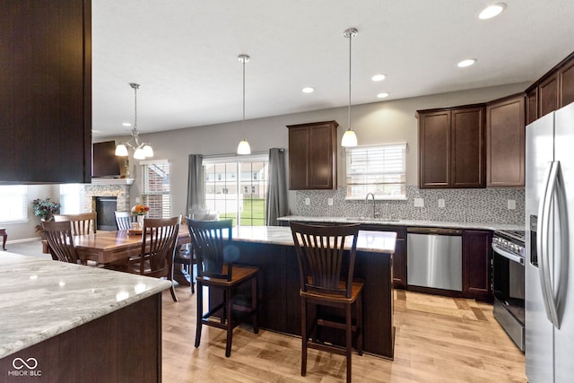 kitchen featuring dark brown cabinetry, a kitchen island, a sink, appliances with stainless steel finishes, and backsplash