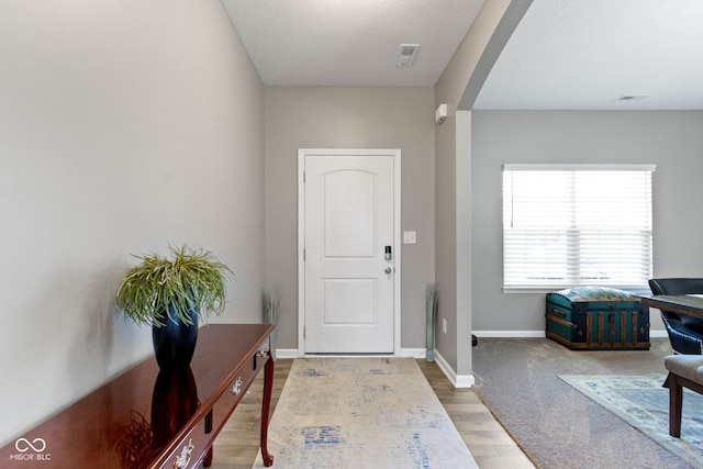 foyer entrance featuring baseboards, arched walkways, and wood finished floors