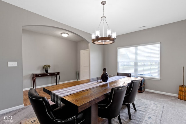 dining space with arched walkways, baseboards, carpet, and a notable chandelier