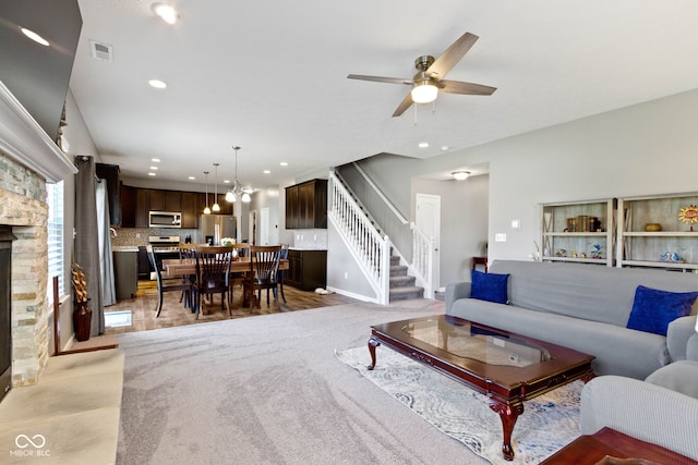 living room featuring ceiling fan, a stone fireplace, visible vents, stairway, and recessed lighting