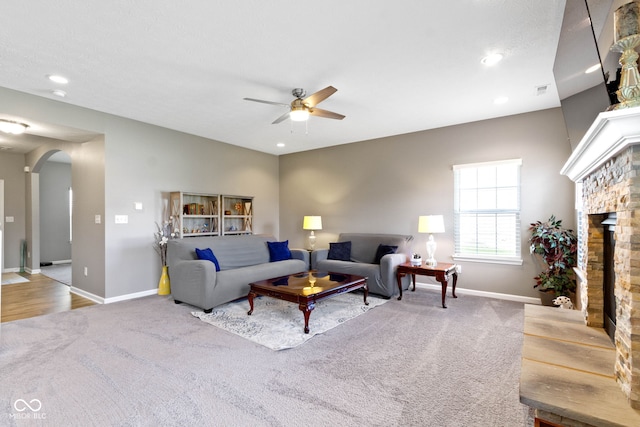 carpeted living area featuring a ceiling fan, arched walkways, a fireplace, baseboards, and recessed lighting