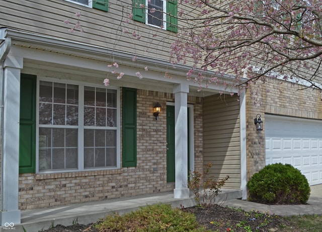 entrance to property with a porch, a garage, and brick siding