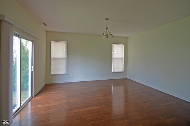 spare room featuring a notable chandelier, dark wood-type flooring, baseboards, and visible vents