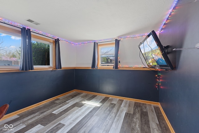 empty room featuring baseboards, wood finished floors, visible vents, and plenty of natural light