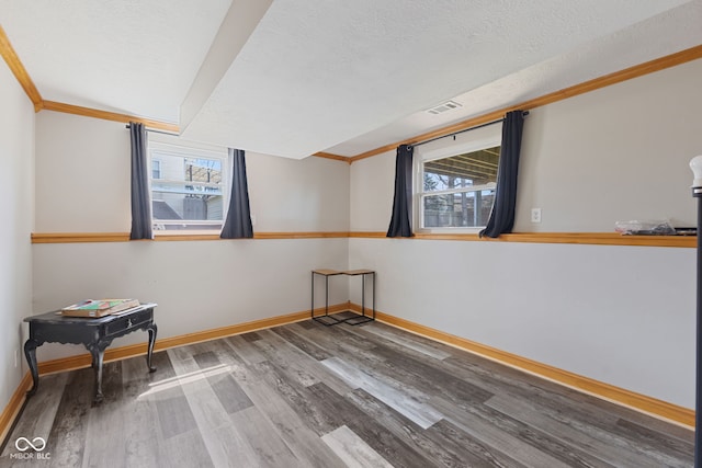 spare room featuring wood finished floors, a textured ceiling, baseboards, and ornamental molding