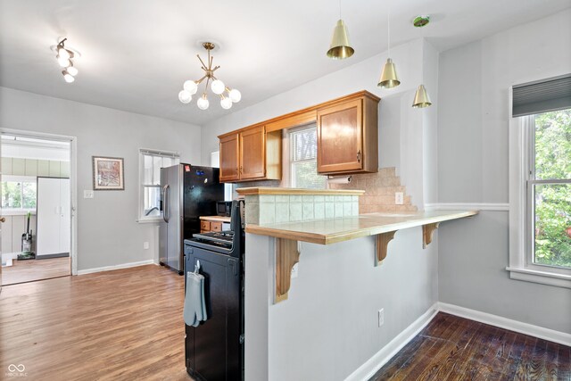 kitchen featuring gas range, a kitchen bar, wood finished floors, brown cabinetry, and baseboards