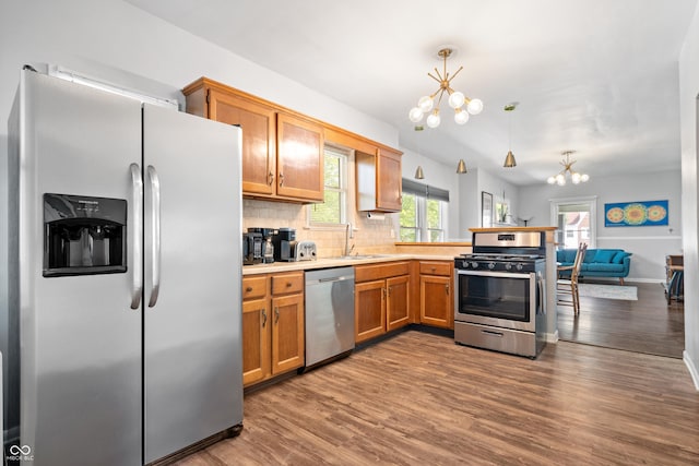 kitchen featuring stainless steel appliances, a chandelier, a sink, a peninsula, and dark wood-type flooring