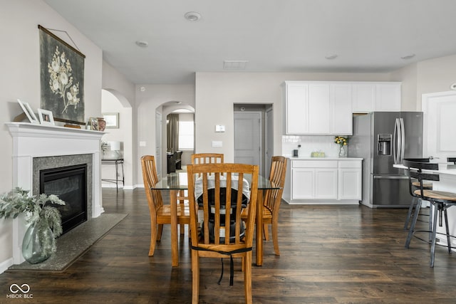 dining area with arched walkways, dark wood finished floors, and a fireplace