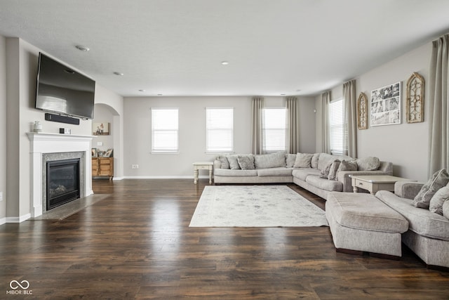living area with arched walkways, baseboards, a fireplace with flush hearth, and wood finished floors
