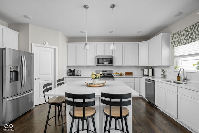 kitchen with a sink, dark wood finished floors, appliances with stainless steel finishes, and a kitchen breakfast bar