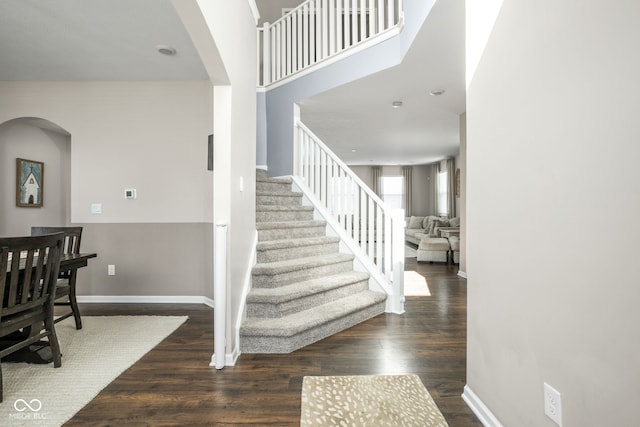 staircase with baseboards, arched walkways, and wood finished floors