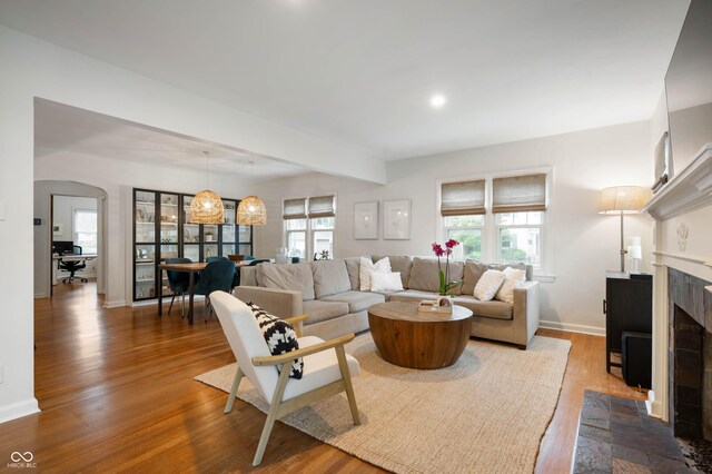 living area featuring a tiled fireplace, wood finished floors, arched walkways, baseboards, and recessed lighting