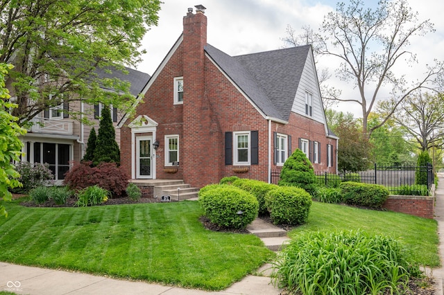 tudor-style house with brick siding, a chimney, and a shingled roof