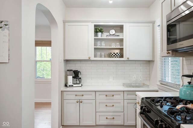 kitchen featuring stainless steel microwave, gas range oven, arched walkways, decorative backsplash, and light countertops