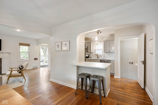 kitchen featuring arched walkways, a kitchen breakfast bar, light countertops, and wood finished floors
