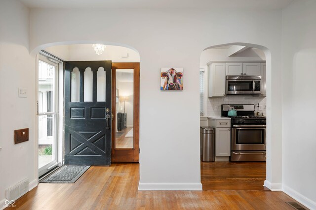 foyer featuring wood finished floors, baseboards, and arched walkways